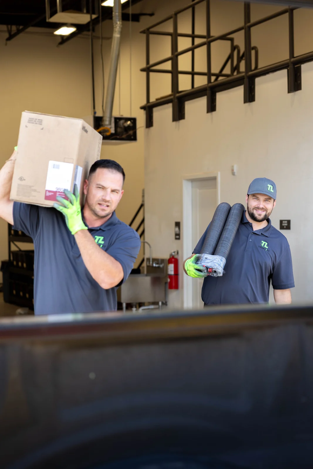 Two True Lift team members carrying a boxed part and coiled garage door parts toward the truck.
