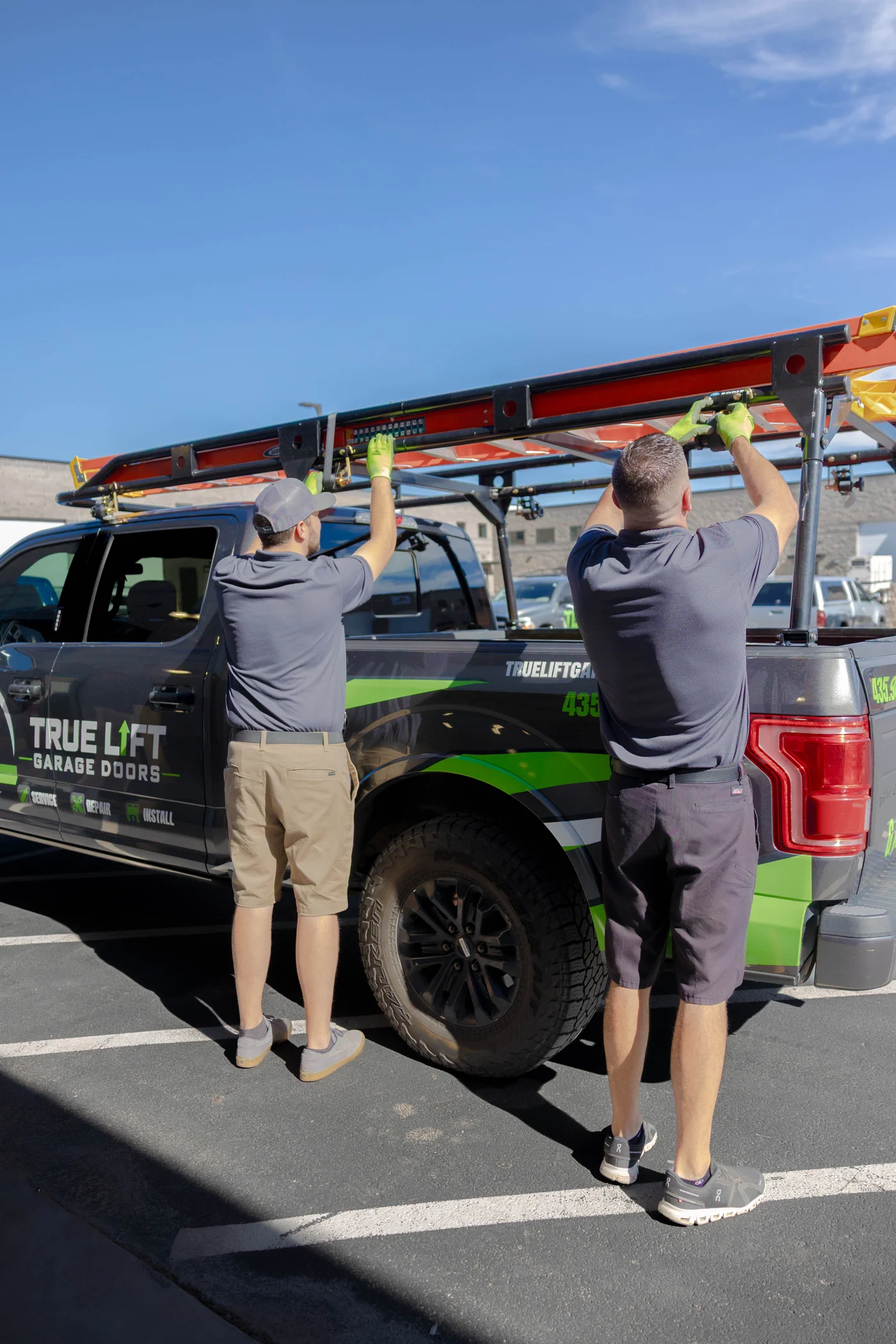 Two True Lift team members securing a ladder to their garage door service truck.