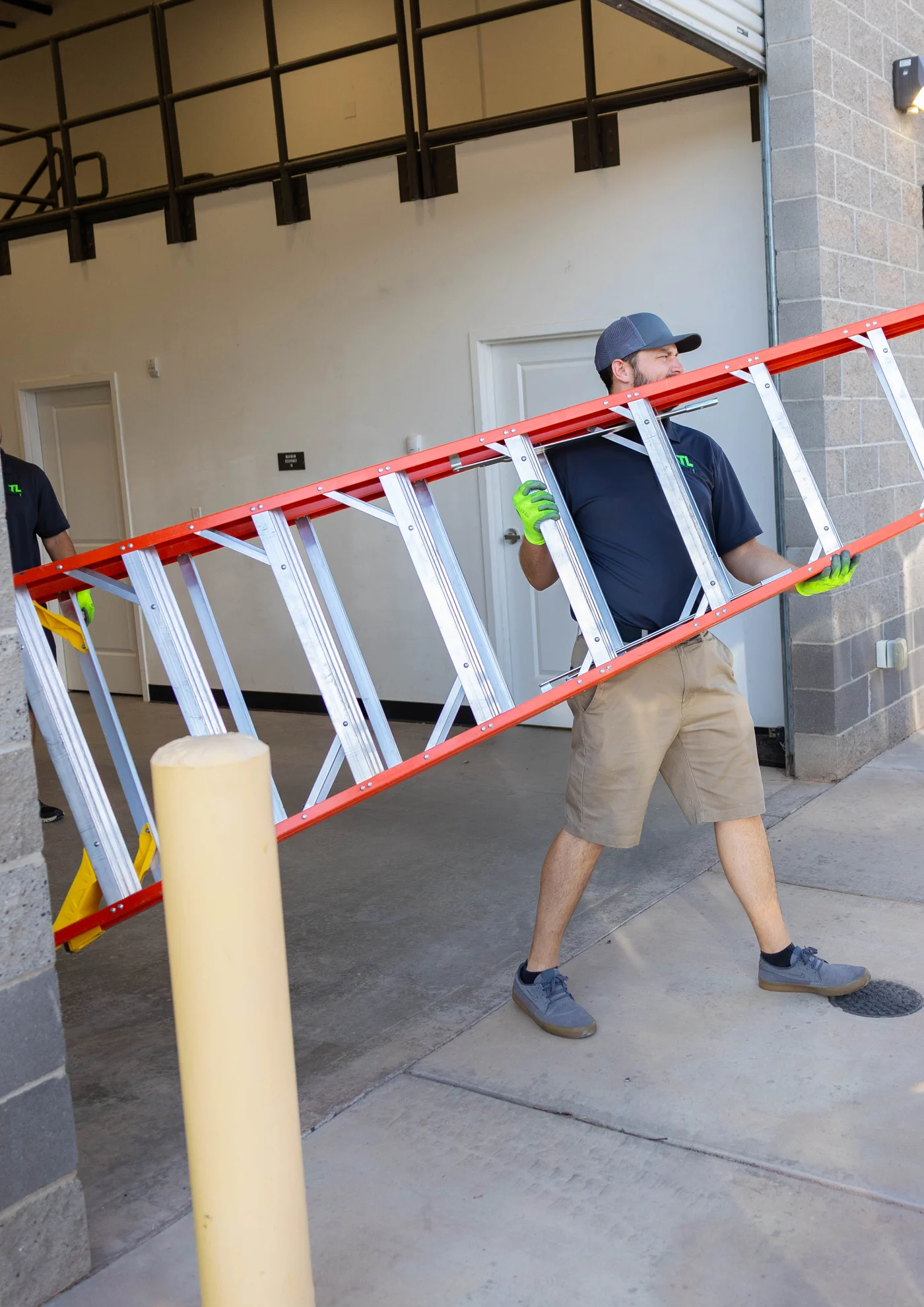 True Lift team member carrying an extension ladder in work gloves.